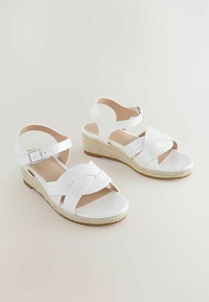 Sandalias espadrilles blancas con tiras cruzadas, hebilla en el tobillo y suela plataforma de yute trenzado. Textura suave con interior beige claro.