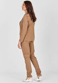 Rjav prugast krojen suknjič z prilagojenim jakno in zoženimi hlačami. V kombinaciji z belimi sandali z odprtimi prsti, ki imajo gladko teksturo tkanine.