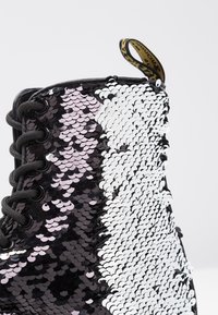 Botín de tobillo en negro y blanco con lentejuelas texturizadas, punta redonda, cordones negros y una cinta en el talón.
