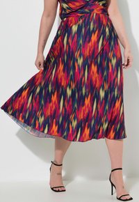 Värikäs, poimuinen midi-mekko, jossa on eläväinen punaisen, oranssin, keltaisen ja sinisen kuosi. Viimeistelty mustilla, hihnallisilla sandaaleilla.