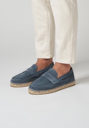 Blaue Wildleder-Slipper mit einer flachen Espadrille-Sohle, die ein gesticktes Design und einen breiten Riemen über dem Vorderfuß aufweisen.