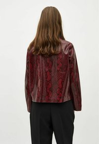 Röd ormskinns-läderjacka med en kroppsnära design, med långa ärmar och en slät textur, i kombination med svarta byxor.