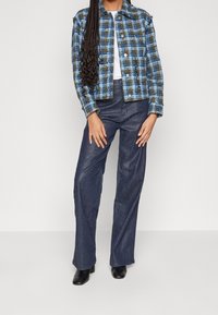 Kariertes Jackett in Blau und Schwarz, mit einem verkürzten Design, Knopfverschluss und zwei Brusttaschen, kombiniert mit dunklen weit geschnittenen Jeans und Stiefeletten.