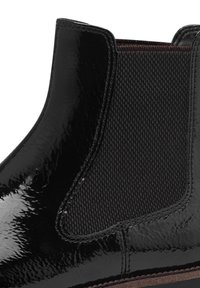 Botte Chelsea noire brillante avec panneau latéral élastique et couture visible au-dessus de la semelle marron.
