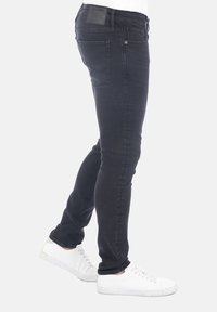 Vaqueros ajustados en denim gris oscuro con un acabado suave. Presentan un bolsillo trasero con costura y una pequeña etiqueta de marca. Llevados con zapatillas blancas.