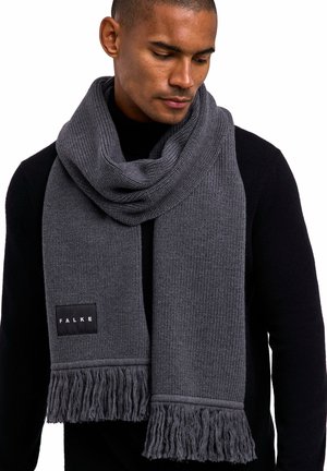 Écharpe en tricot grise avec des extrémités frangées et un motif texturé, arborant une étiquette noire avec le logo "FALKE", portée sur un pull noir.
