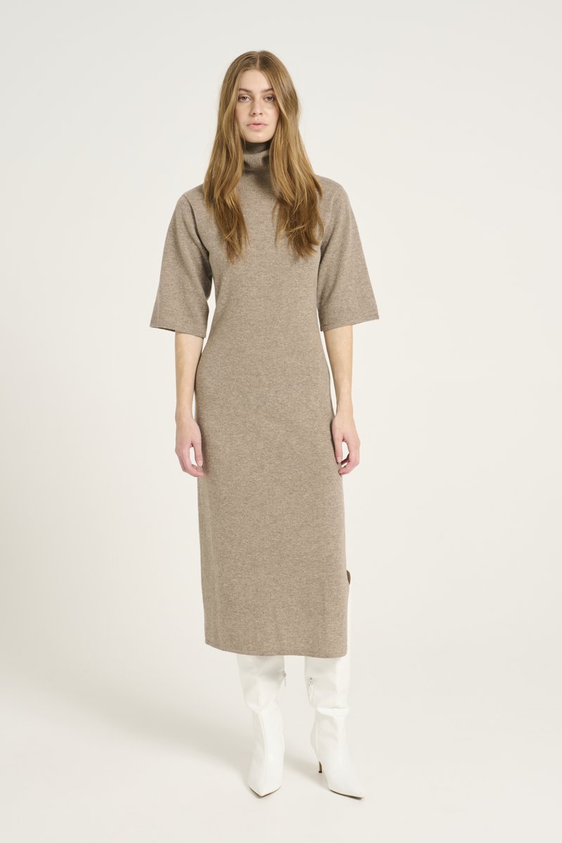 Lungo vestito beige a maglia con collo alto, maniche corte e spacchi laterali. Abbinato a stivali bianchi con punta a punta per un contrasto.