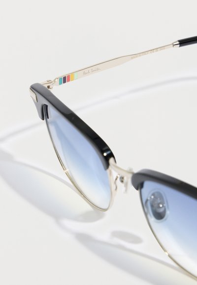 Ochelari de soare cu ramă din plastic negru, lentile degradate albastre și accente argintii. Au o dungi multicolore pe braț, gravată cu "Paul Smith".