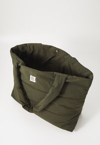 Sac fourre-tout rembourré vert olive avec deux poignées, fermeture à bouton-pression et patch logo sur le côté. texture de tissu douce avec un design matelassé.