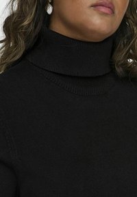 Črn pulover s turtleneck iz ribane tkanine in visokim ovratnikom, ki vsebuje diskretno šivanje ob ramenih.