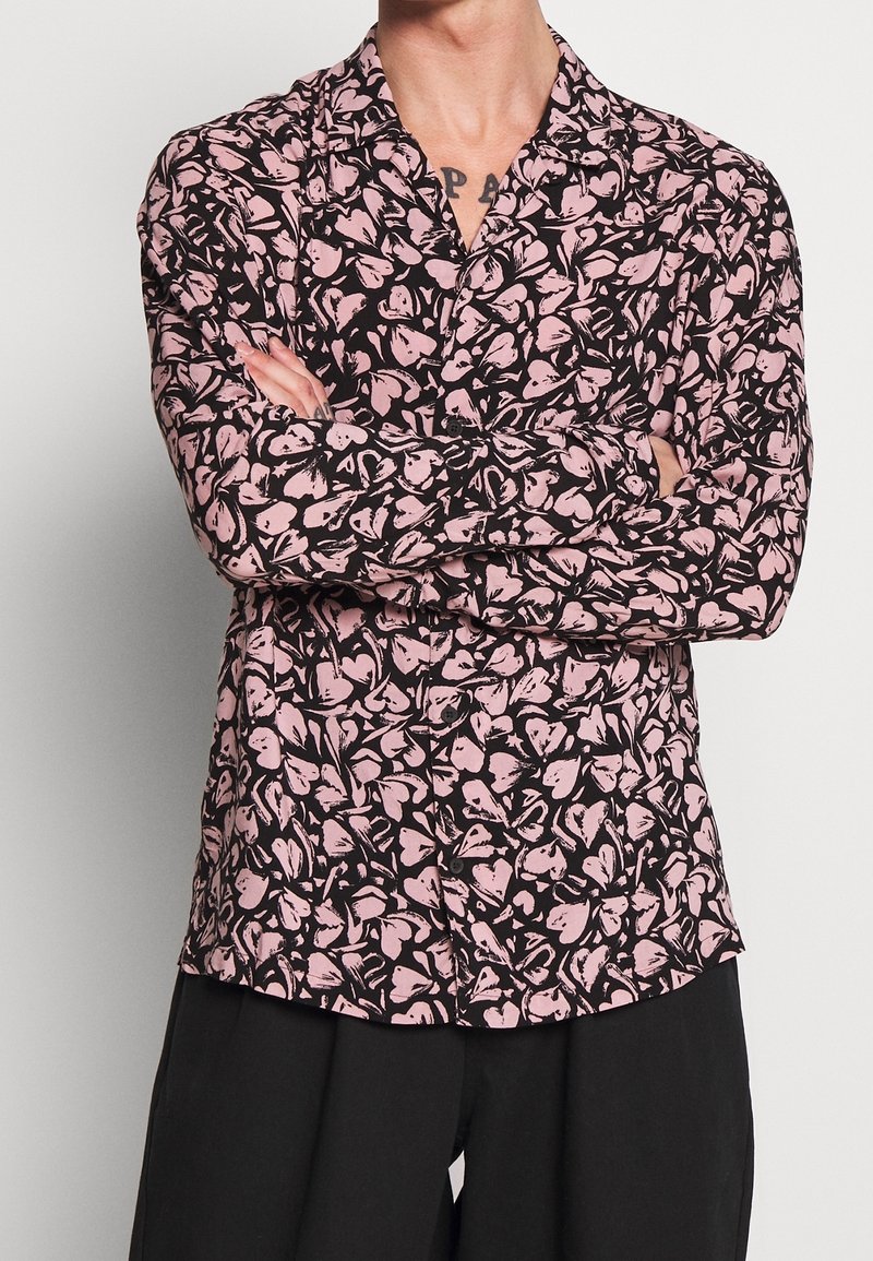 Svart skjorta med rosa blommönster, långa ärmar, krage och knappframsida. Tyget verkar slätt med en lätt textur.