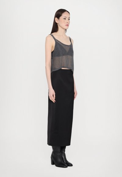 Grijze cropped tanktop met doorschijnende textuur, gecombineerd met een zwarte, lange rok tot de vloer. Model draagt zwarte, hoge laarzen. Eenvoudig, modern ontwerp.