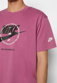 Lila bomull t-shirt med en djärv svart Nike-logotyp i mitten och en mindre logotyp på ärmen. Rund hals och korta ärmar.