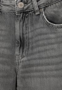 Szare dżinsy mają zapięcie na guzik, przednie kieszenie oraz lekko wyblakłą teksturę z widocznymi detalami szwów.