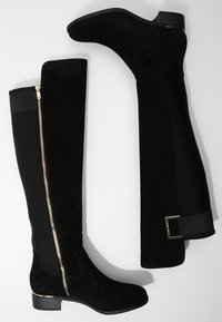Black knee-high boots featuring a suede finish, gold zipper detail, elastic panel, and a low block heel. Smooth texture with minimal accents.