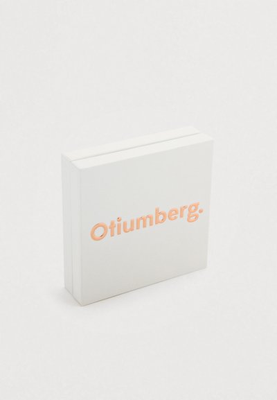 Boîte rectangulaire blanche avec une surface texturée, présentant le nom de la marque "Otiumberg" en lettres en relief de couleur pêche.