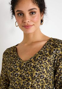 Vestido de tela con estampado floral que presenta un escote en V, mangas largas, en tonos de verde, negro y blanco con detalles texturizados.