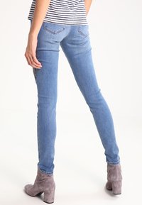 Fittade blå denimjeans med bakfickor, i kombination med grå ankelskorna. Tyget har lätt slitna detaljer längs sömmarna.