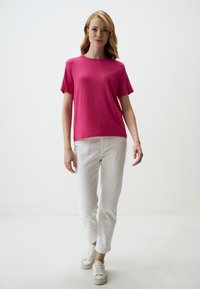 Fuchsia T-shirt met korte mouwen, gemaakt van zachte stof, gecombineerd met witte rechte broek en witte sneakers tegen een neutrale achtergrond.