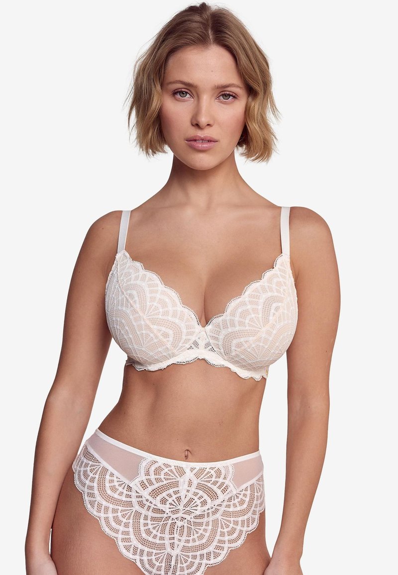 Set di reggiseno in pizzo e slip coordinati in soffice crema. Motivo floreale in pizzo con bordi smerlati, dotato di spalline regolabili e dettagli delicati rifiniti.