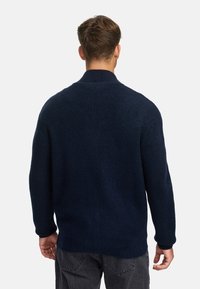 Jersey de punto azul marino con textura acanalada, que presenta un cuello alto y mangas largas, visto desde la parte posterior.