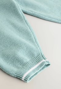 Helles blaues Strickgewebe mit strukturiertem Finish; verfügt über einen gerippten Bund mit weißen Streifen und zeigt weiches, bequemes Material.