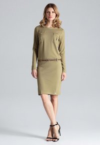 Khaki sukienka z długim rękawem, dwiema przednimi kieszeniami, dopasowaną talią i brązowym paskiem. Gładki materiał i długość do kolan. Czarne sandały na obcasie.