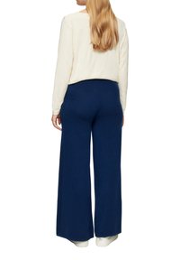 Navy wijdere broek van gestructureerde stof, gecombineerd met een lichtromige lange mouwen top. De outfit heeft een relaxte pasvorm en zachte materialen.