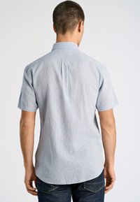 Camisetta azzurra a maniche corte con una sottile texture, colletto a camicia e orlo curvo, indossata con jeans scuri.