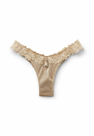Beiger Satin-Tanga mit floraler Spitzenbund und kleinem dekorativem Anhänger vorne in der Mitte vor weißem Hintergrund.