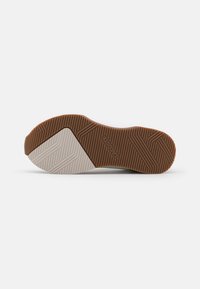 Kengän pohja ruskealla ja beiging kumilla, tekstuurilla varustetut pito-kuviot, ja "Lacoste" -merkin nimi painettuna lähelle keskustaa.