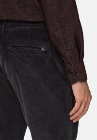 Ciemne spodnie kordurowe w pionowe paski, z detalami na tylnej kieszeni, zestawione z fakturowaną brązową koszulą z długim rękawem i zapiętymi mankietami.