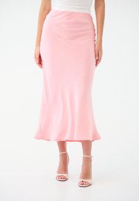 Gonna in satin rosa chiaro, a lunghezza ginocchio, con una silhouette morbida e una leggera svasatura sull'orlo. Un paio di tacchi bianchi con cinturino alla caviglia.