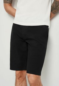 Czarne bawełniane szorty o luźnym kroju, z przednimi kieszeniami i gładką fakturą. Stylizowane z prostą białą koszulą u góry.