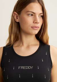 Top senza maniche nero realizzato in morbido tessuto, con strass argentati disposti attorno al nome del marchio "FREDDY" al centro.