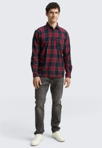 Rot und marineblau kariertes Flanellhemd mit Knopfleiste, langen Ärmeln und einer einzelnen Brusttasche, kombiniert mit grauen Jeans und weißen Sneakers.