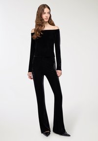 Czarny welurowy top na ramiączkach z długimi rękawami w połączeniu z dopasowanymi czarnymi spodniami w kształcie dzwonów, tworząc elegancki, spójny wygląd.