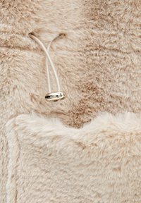 Blød beige imiteret pelsmateriale med en luksuriøs tekstur. Har en snor med en metallisk stopper til justering.