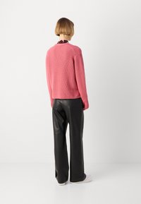 Rožinė raukinėta megztinis su ilgomis rankovėmis, derinama su juodomis odinėmis plačiomis kelnėmis. Pavaizduota iš nugaros, rodanti neformalią, laisvą išvaizdą.