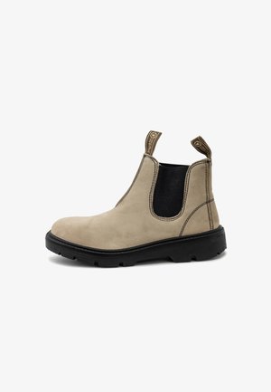 Botte Chelsea en suede beige avec des panneaux élastiques noirs sur les côtés, des languettes de tirage et une semelle en caoutchouc. Présente des coutures contrastées et une pointe arrondie.