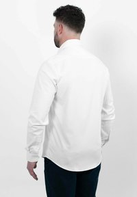 Witte blouse met lange mouwen, een afgeronde onderkant, knopenmanchetten en een strakke kraag. Gladde stoftextuur zonder zichtbare patronen of accenten.