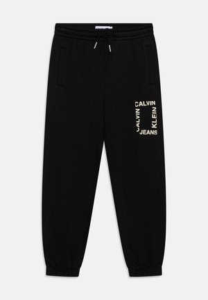 Pantalon de survêtement noir avec taille et poignets élastiques, poches latérales, et logo "Calvin Klein Jeans" imprimé en beige sur la cuisse droite.