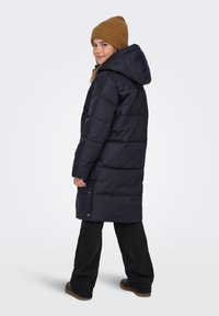 Temno modra puhovka z ruto, s prešito zasnovo in stranskimi žepki s pritiskači, kombinirana s rjavim rebrastim pletenim klobukom.