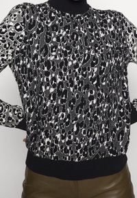 Pull à imprimé léopard en noir et blanc avec un col et des poignets côtelés, confectionné dans un tissu tricoté texturé et une coupe ajustée.