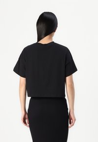 Černé zkrácené tričko s krátkým rukávem, kulatým výstřihem a hladkým bavlněným materiálem, kombinované s přiléhavou černou sukní.