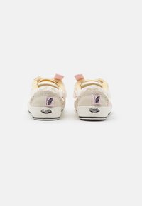 Světlé plátěné tenisky s texturovanými detaily, v pastelově žluté a růžové barvě, s černou gumovou podrážkou. Obsahují logo na patě.