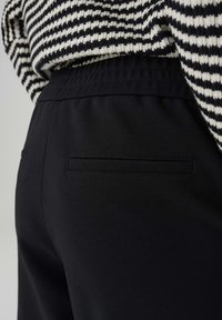 Black pants with a textured finish, featuring an elastic waistband and a single stitched back pocket, paired with a black and white striped top.