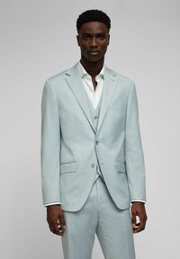 Hellblaues dreiteiliges Anzugset aus strukturiertem Stoff. Blazer mit zwei Knöpfen, mit Revers und passender Weste. Darunter ein weißes Hemd.