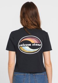 Czarna krótka koszulka z okrągłym wzorem z falistymi paskami w niebieskim, złotym i różowym kolorze, z napisem "volcom stone" na środku.