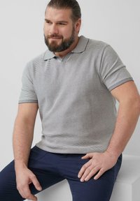 Grijze polo met korte mouwen en lichte strepen, voorzien van een platte kraag. Draagt comfortabel met marineblauwe broek en heeft een aansluitende pasvorm en zachte textuur.